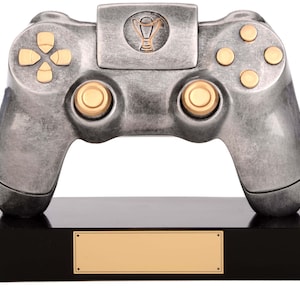 Könnte beinhalten: Silberfarbener Videospiel-Controller-Pokal mit einem goldfarbenen Pokal auf der Vorderseite. Der Pokal steht auf einem schwarzen Sockel mit einer goldfarbenen Plakette.