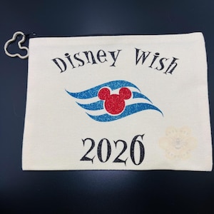 May include: Cream-colored zippered pouch with the words "Disney Wish" above a blue and red Mickey Mouse design and the year "2026". The zipper pull is a Mickey Mouse silhouette.