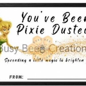 May include: A rectangular sign with a black frame featuring a yellow-haired fairy in a green dress on the left. The text reads You've Been Pixie Dusted, Busy Bee Creations, Spreading a little magic to brighten your day!, and FROM: with a line.