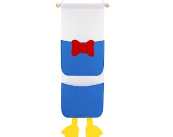May include: A wall hanging organizer shaped like Donald Duck. The organizer features a white top, blue body with a red bow tie, and yellow feet. It is designed to hang from a wooden dowel.