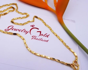 May include: A gold-colored necklace with rectangular links and a hook clasp. The necklace is displayed on a white surface with the text "Jewelry Gold Thailand". A vibrant orange flower is in the background.