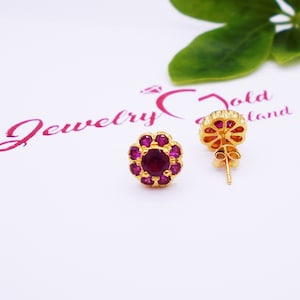 May include: A pair of gold earrings with a flower design. The earrings have a red center stone and are surrounded by smaller red stones.