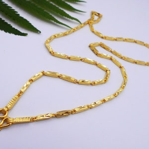 May include: A gold chain necklace with a diamond-shaped pattern. The chain is made of small, linked pieces that are all the same size and shape.