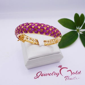 May include: A gold bangle bracelet with a delicate filigree design and a row of pink oval-shaped gemstones.