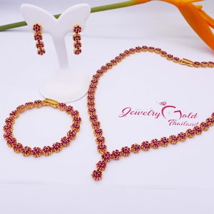 May include: A gold necklace, bracelet, and earrings set with red ruby stones. The necklace has a pendant with a Y-shaped design. The jewelry is on a white background.