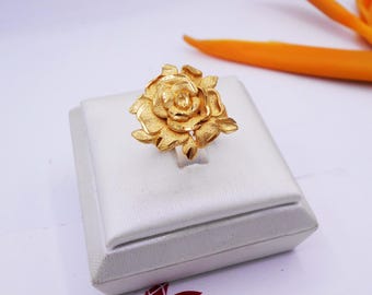 May include: A gold-colored ring with a rose design. The ring is displayed on a white box.