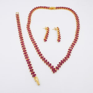 May include: A gold necklace, bracelet, and earrings set with red ruby stones. The necklace has a V-shaped design.