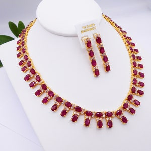 May include: A gold necklace and earrings set with red oval-shaped stones and smaller white stones. The necklace has a delicate design with the stones set in a row.