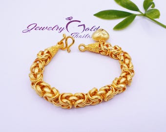 Könnte beinhalten: Ein goldfarbenes Armband mit geflochtenem Design. Das Armband hat einen herzförmigen Anhänger und einen Hakenverschluss. Im Hintergrund steht "Jewelry Gold Thailand". Das Armband ist etwa 18 cm lang.