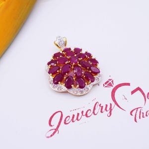 Peut inclure: Un pendentif en or avec un motif de fleur orné de pierres rubis rouges et de diamants blancs. Le pendentif est sur un fond blanc avec le texte "Jewelry Gold Thailand".