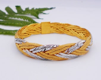 Könnte beinhalten: Ein goldfarbenes Armband mit geflochtenem Design. Das Armband hat eine Kombination aus gold- und silberfarbenem Metall, das miteinander verwoben ist. Der Verschluss hat eine einfache rechteckige Form. Das Armband hat einen Durchmesser von ca. 6,35 cm.