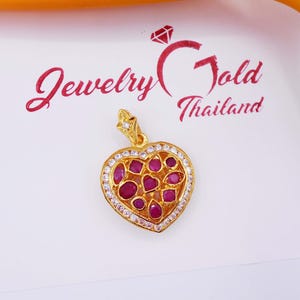 May include: A gold heart-shaped pendant with a white border and red gemstones. The pendant is on a white background with the text "Jewelry Gold Thailand".