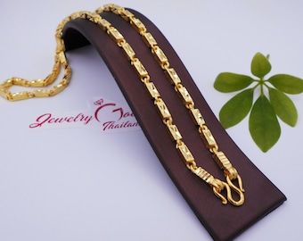 May include: A gold-colored necklace with a rectangular link design is displayed on a brown jewelry stand. The necklace is made of multiple rectangular links. The jewelry stand is on a white surface. The text "Jewelry God Thailand" is visible.