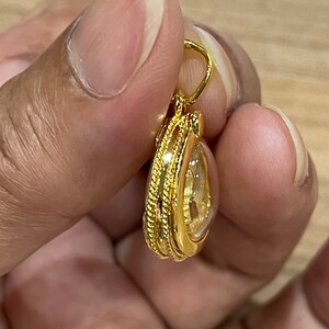 K&ouml;nnte beinhalten: Ein goldener Anh&auml;nger mit einem klaren Stein im Inneren. Der Anh&auml;nger hat eine seilartige Umrandung.