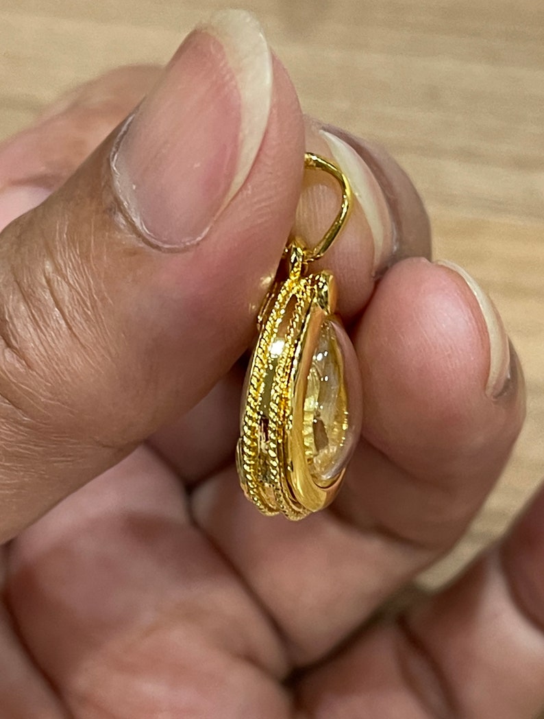 K&ouml;nnte beinhalten: Ein goldener Anh&auml;nger mit einem klaren Stein im Inneren. Der Anh&auml;nger hat eine seilartige Umrandung.