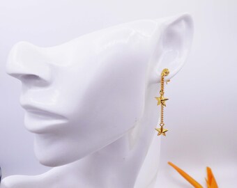 May include: Gold star dangle earrings with a chain and three star charms. The earrings are shown on a white mannequin head.