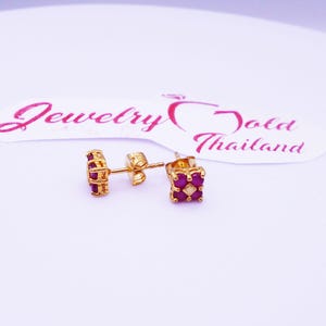 May include: A pair of gold earrings with a square design featuring multiple small red gemstones.
