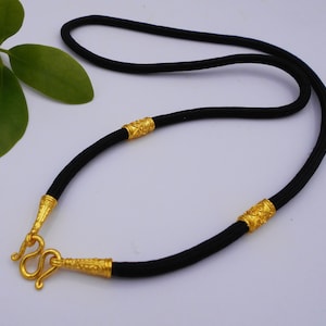May include: A black cord necklace with gold accents. The necklace has a hook clasp and two gold beads with intricate designs.