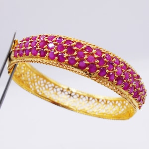 May include: A gold bangle bracelet with a delicate filigree design and a row of pink ruby stones.