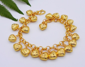 Puede incluir: Un brazalete de oro con un diseño de cadena de eslabones y múltiples dijes en forma de corazón. Los dijes son texturizados y tienen un diseño ligeramente elevado.