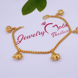 May include: Gold chain bracelet with five small elephant charms. The bracelet is on a white background. Jewelry Gold Thailand.