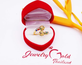 May include: A gold ring with two colorful enamel balls. The ring is in a red velvet ring box. The box is on a white surface.