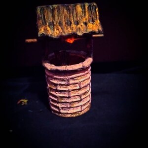 May include: A small, decorative well made of brown and pink painted cardboard. The well has a wooden roof and a small opening at the top.