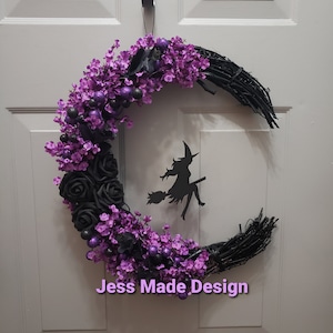 May include: A black crescent moon wreath decorated with purple flowers, black roses, and purple glitter balls. A black silhouette of a witch flying on a broomstick is in the center of the wreath. The wreath is labeled "Jess Made Design".