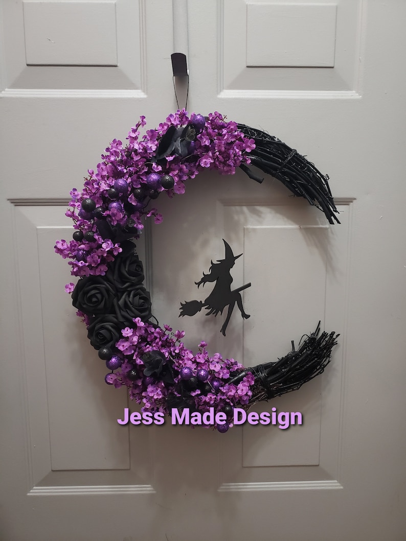 May include: A black crescent moon wreath decorated with purple flowers, black roses, and purple glitter balls. A black silhouette of a witch flying on a broomstick is in the center of the wreath. The wreath is labeled "Jess Made Design".
