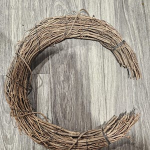 May include: A crescent-shaped wreath crafted from intertwined brown twigs. The natural, rustic design is held together with black bands. This decorative piece is suitable for seasonal or year-round home decor.