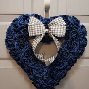 K&ouml;nnte beinhalten: Ein herzf&ouml;rmiger Kranz aus blauen Stoffrosen mit einer grauen und wei&szlig;en Gingham-Schleife.