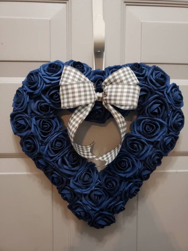 K&ouml;nnte beinhalten: Ein herzf&ouml;rmiger Kranz aus blauen Stoffrosen mit einer grauen und wei&szlig;en Gingham-Schleife.