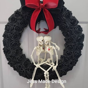 May include: A black rose wreath with a red and black bow, and two skeleton figures. The wreath is decorated with black roses and has a red heart on each skeleton's chest. The text "Jess Made Design" is visible.