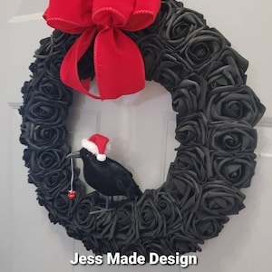May include: A black rose wreath with a red velvet bow and a black crow wearing a Santa hat holding a red ornament.