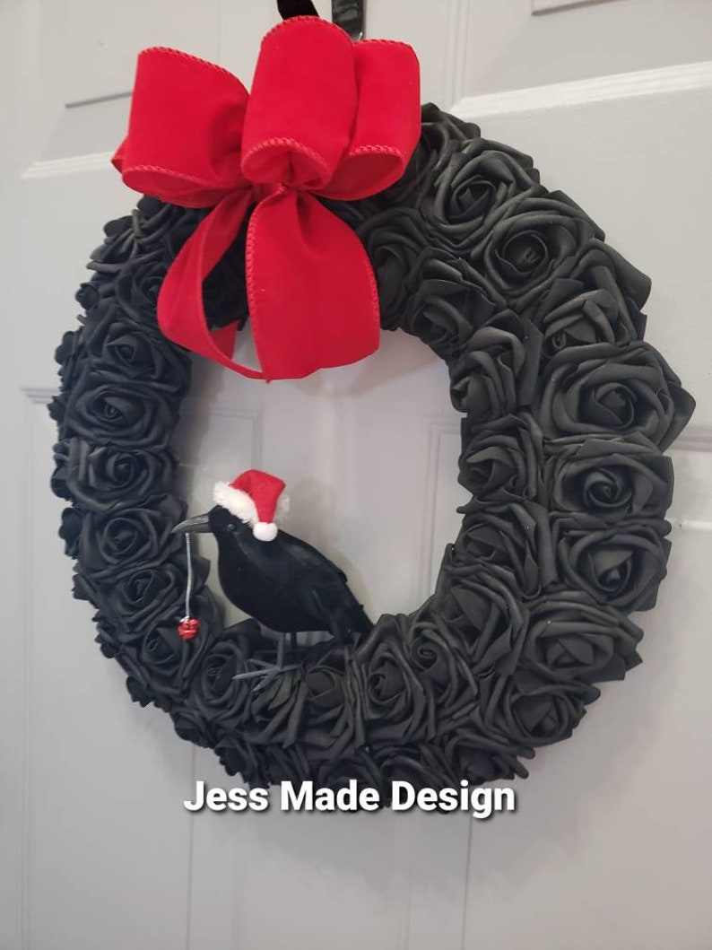 May include: A black rose wreath with a red velvet bow and a black crow wearing a Santa hat holding a red ornament.