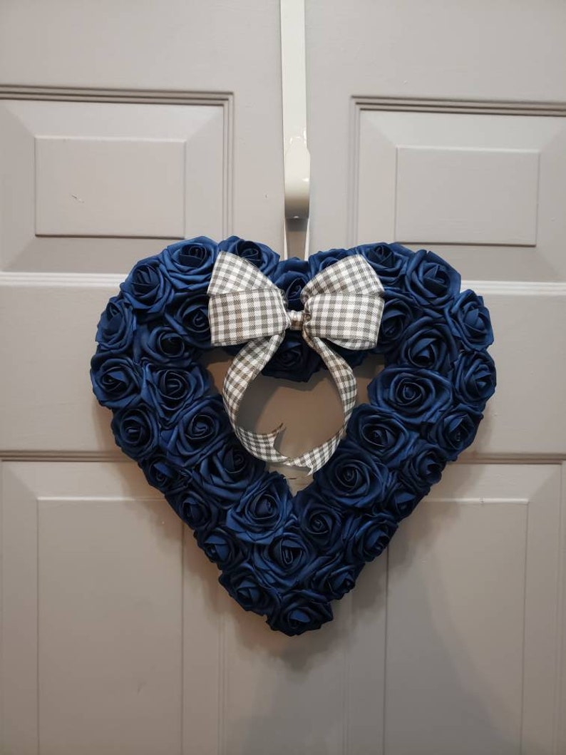 K&ouml;nnte beinhalten: Ein herzf&ouml;rmiger Kranz aus blauen Stoffrosen mit einer wei&szlig;en und grauen Gingham-Schleife.