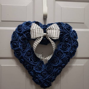 K&ouml;nnte beinhalten: Ein herzf&ouml;rmiger Kranz aus blauen Stoffrosen mit einer wei&szlig;en und grauen Gingham-Schleife.