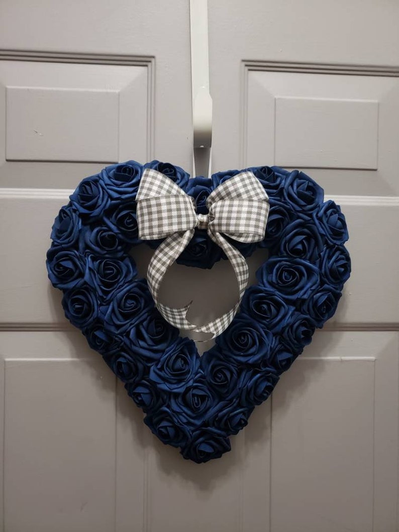 K&ouml;nnte beinhalten: Ein herzf&ouml;rmiger Kranz aus blauen Stoffrosen mit einer wei&szlig;en und grauen Gingham-Schleife.