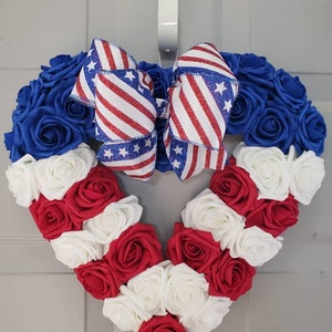 May include: Heart-shaped wreath with blue, red, and white roses, resembling the American flag. A patriotic bow with red and white stripes and blue stars adorns the top. Perfect for Independence Day or other patriotic holidays.