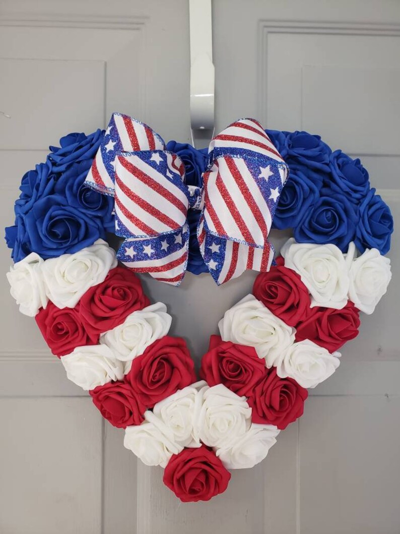 May include: Heart-shaped wreath with blue, red, and white roses, resembling the American flag. A patriotic bow with red and white stripes and blue stars adorns the top. Perfect for Independence Day or other patriotic holidays.