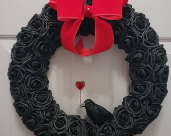 May include: A black rose wreath with a red velvet bow and a black crow holding a red heart.