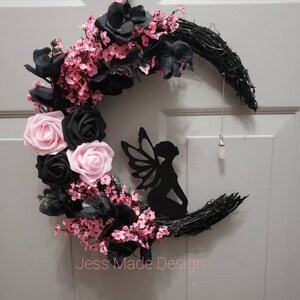 May include: A black and pink crescent moon wreath with a fairy silhouette and pink flowers. The wreath is made of twigs and has a black ribbon hanging from it. The text "Jess Made Design" is visible at the bottom of the image.
