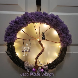 May include: A purple and black Halloween wreath with a skeleton on a swing, a black cat, and a tree with lights. The wreath has the text "Jess Made Design" at the bottom.