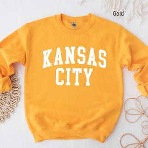 May include: A gold sweatshirt with the text "KANSAS CITY" in white letters.