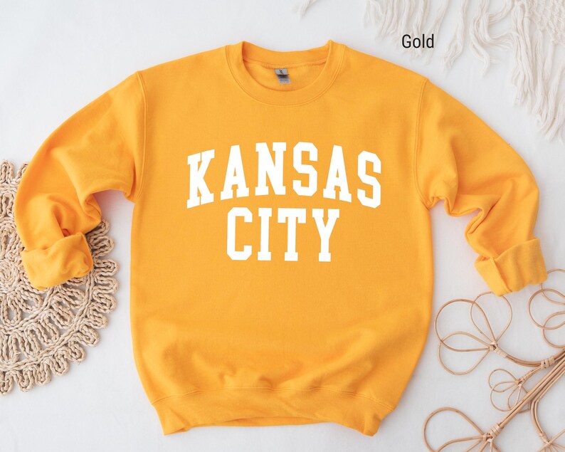 May include: A gold sweatshirt with the text "KANSAS CITY" in white letters.