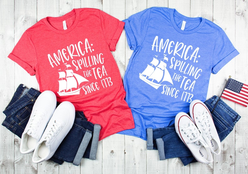 May include: Two t-shirts with a red and blue color scheme. The shirts feature a white graphic of a ship with the text "America: Spilling the Tea Since 1773".