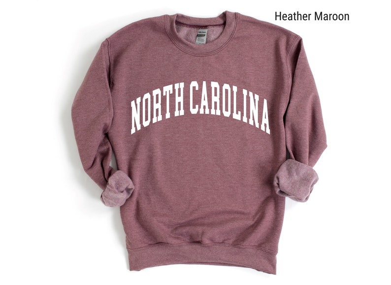 Pode incluir: Uma camisa de moletom marrom com o texto "NORTH CAROLINA" impresso em branco.
