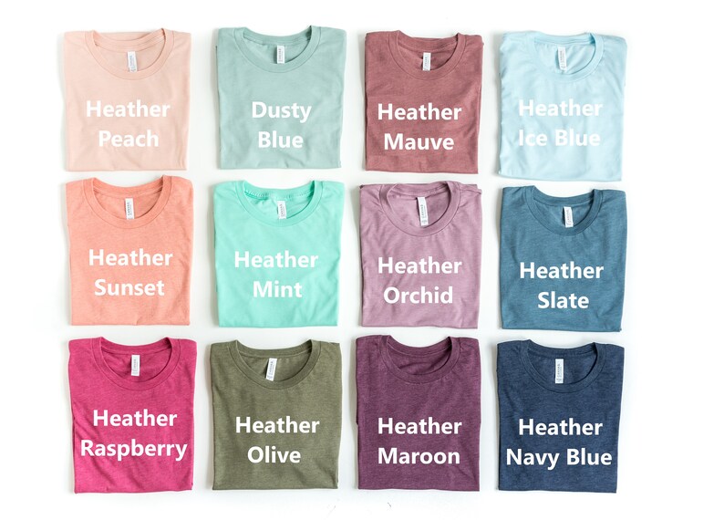 May include: Twelve folded t-shirts in various heather colors, including peach, dusty blue, mauve, ice blue, sunset, mint, orchid, slate, raspberry, olive, maroon, and navy blue.