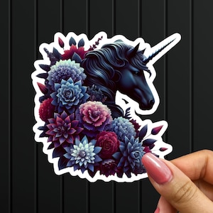 May include: A black unicorn with a single horn is surrounded by a wreath of dark purple, blue, and red flowers. The unicorn's head is turned to the side, and its eye is visible. The flowers are arranged in a circular pattern around the unicorn's head.