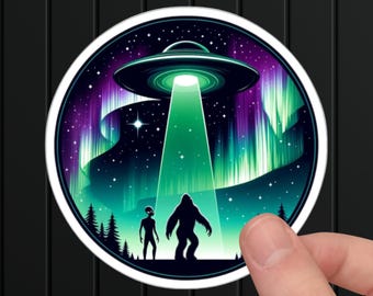 May include: A round sticker with a black silhouette of a Bigfoot and an alien standing in front of a green and purple aurora borealis. A flying saucer hovers above them, casting a green beam of light.